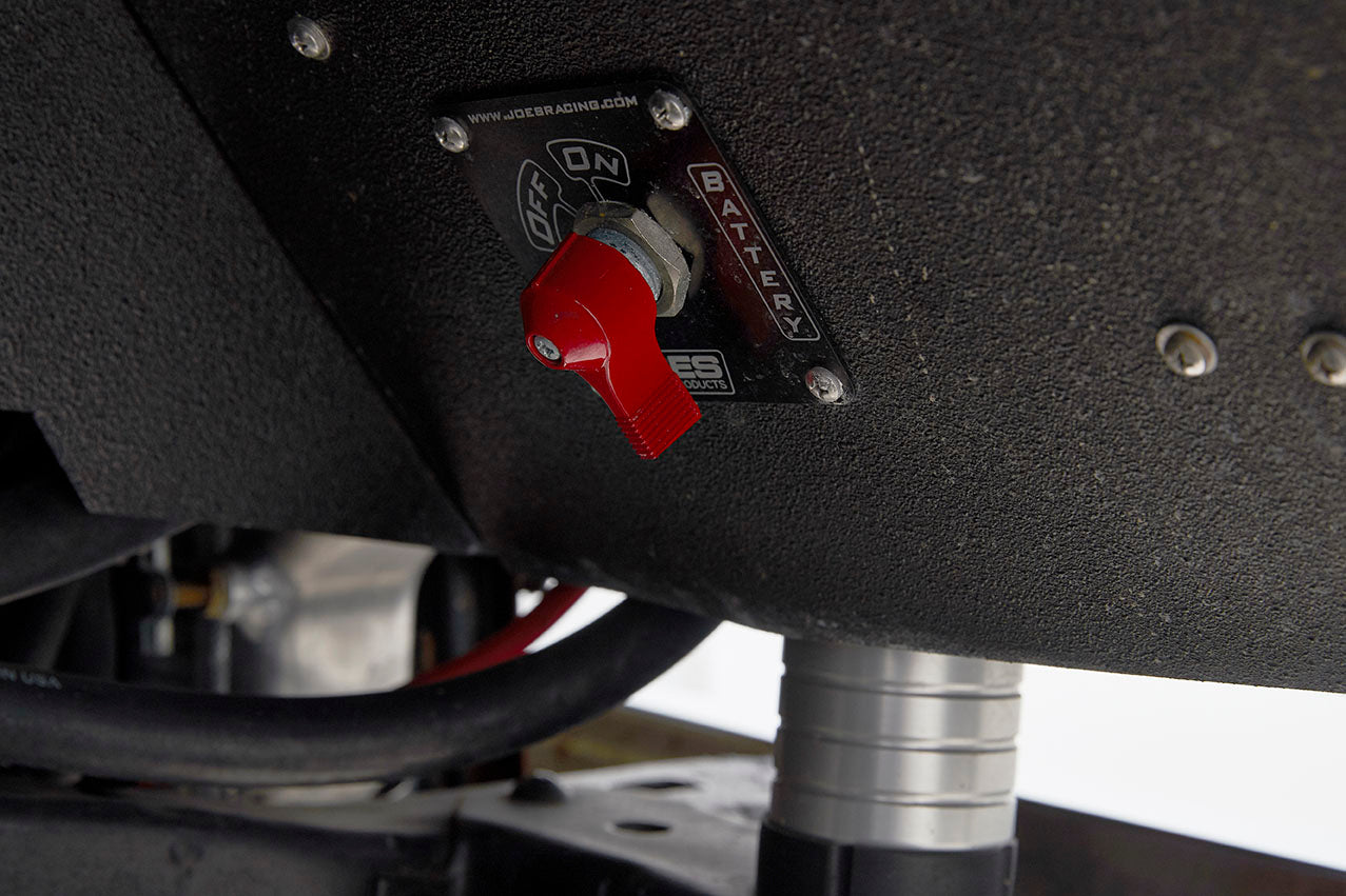 Close-up of a red toggle switch labeled for battery on a black textured panel under vehicle