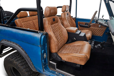 Inside view showing diamond-stitched brown leather front bucket seats in a blue Classic Ford Bronco
