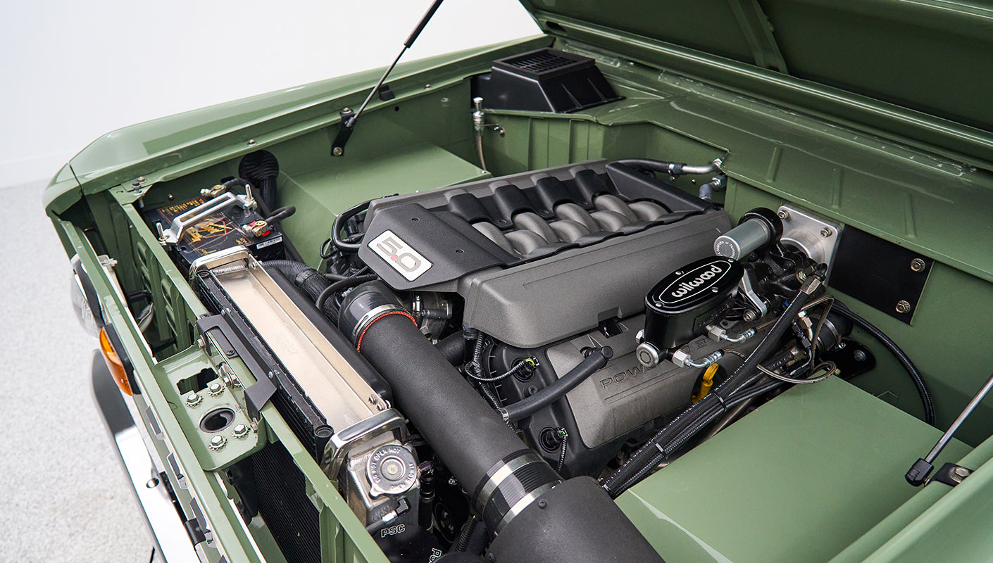 Wide view of 5.0 liter Ford engine and related parts inside green engine bay of Classic Ford Bronco