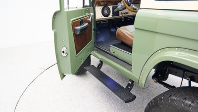Side view of open driver door with black running board and green body of Classic Ford Bronco