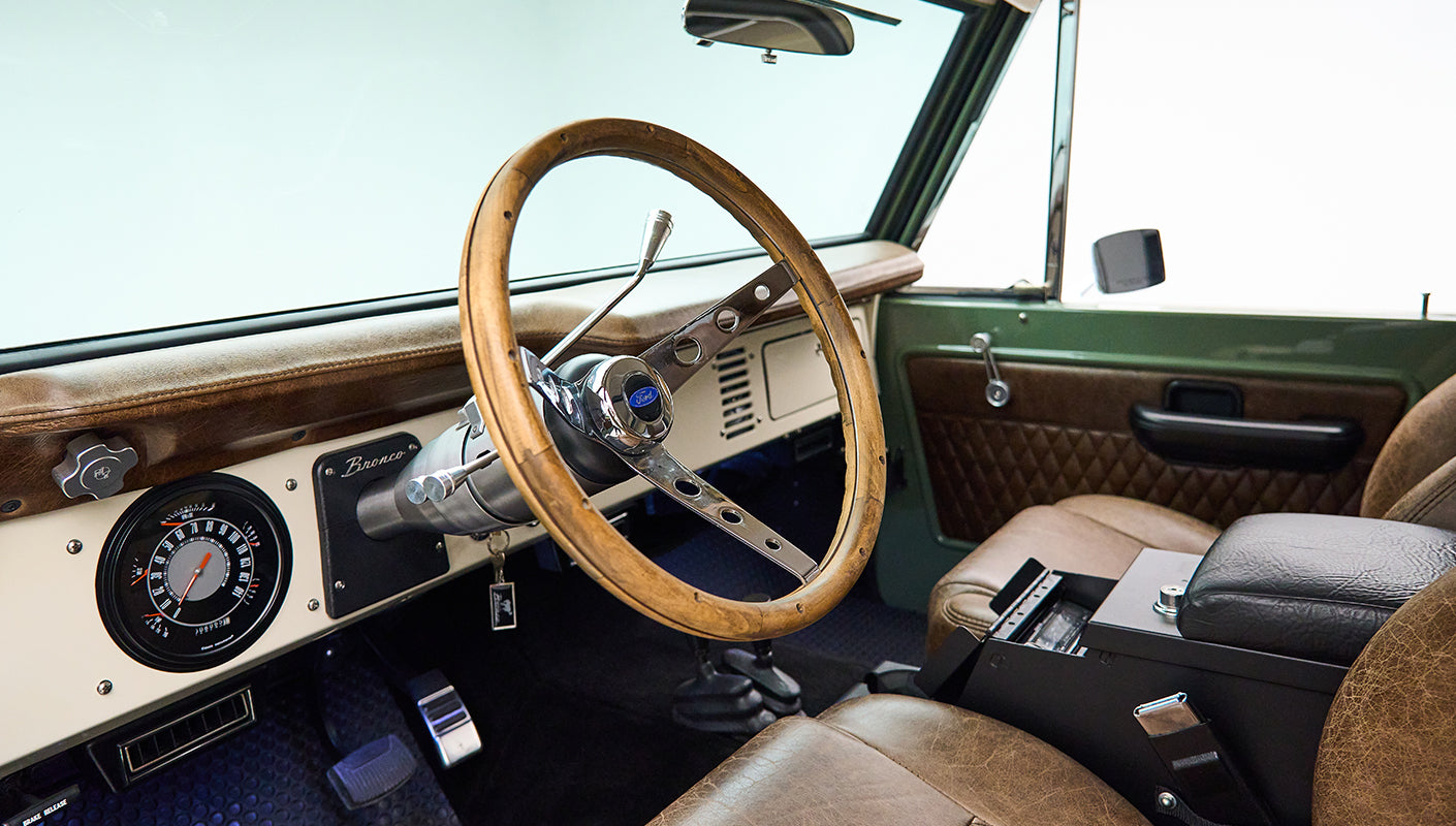 Classic Ford Bronco interior showing wooden steering wheel and dashboard with speedometer