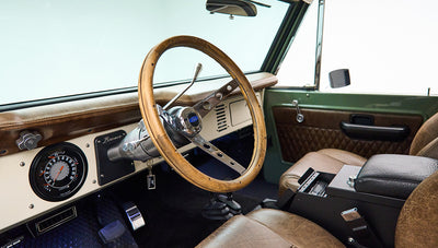 Classic Ford Bronco interior showing wooden steering wheel and dashboard with speedometer
