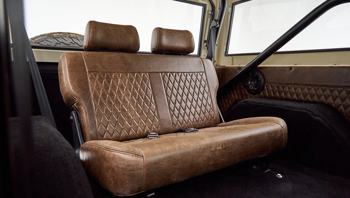 Brown leather rear bench seat with diamond stitching in Classic Ford Bronco with visible roll cage and speaker