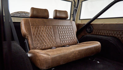 Brown leather rear bench seat with diamond stitching in Classic Ford Bronco with visible roll cage and speaker