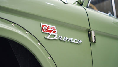 Close-up of classic Bronco front grille with round headlights and FORD badge in red letters.