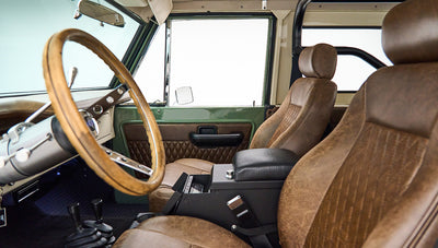 Interior driver side of Classic Ford Bronco with worn brown leather seats and wooden steering wheel