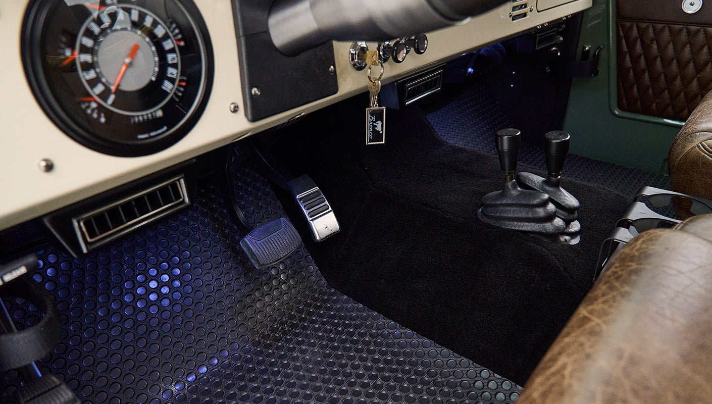Classic Ford Bronco interior with black pedals, stick shifts, and dashboard controls with nearby key