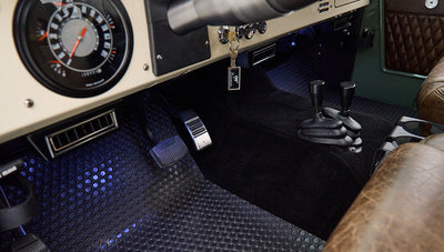 Classic Ford Bronco interior with black pedals, stick shifts, and dashboard controls with nearby key