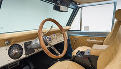 Classic Ford Bronco driver seat and dashboard with wooden steering wheel and beige upholstery.