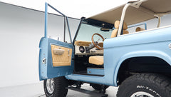 Side profile of Classic Ford Bronco with open driver door revealing beige interior and blue exterior.