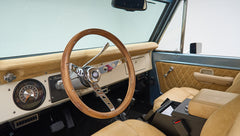 Classic Ford Bronco driver seat and dashboard with wooden steering wheel and beige upholstery.