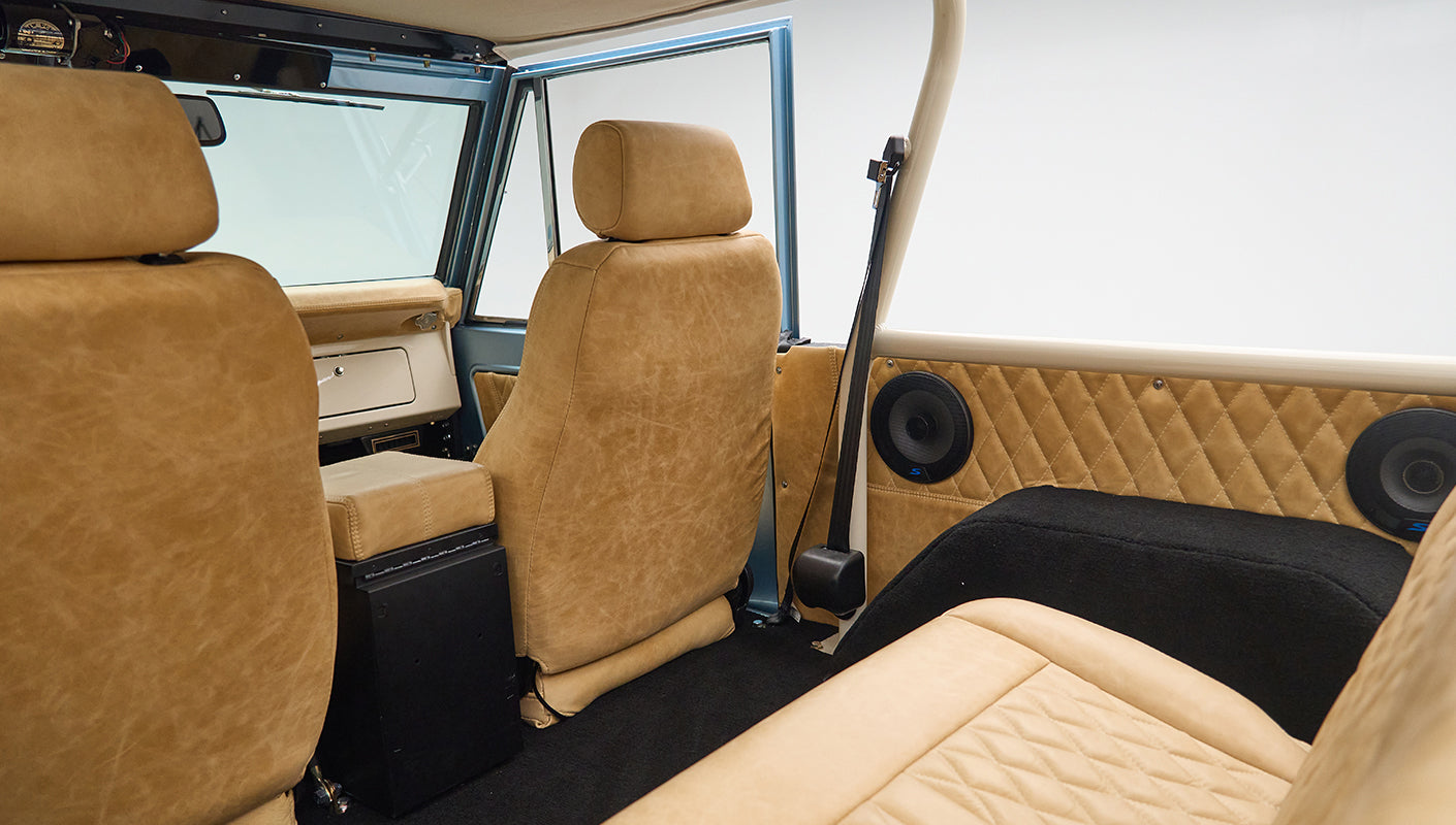 Rear interior view of Classic Ford Bronco with beige leather seats and open side door.