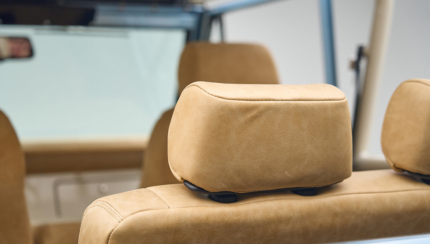 Interior shot focused on tan leather headrest and seat of Classic Ford Bronco with roll cage frame visible
