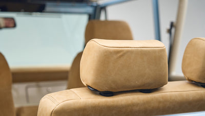 Interior shot focused on tan leather headrest and seat of Classic Ford Bronco with roll cage frame visible