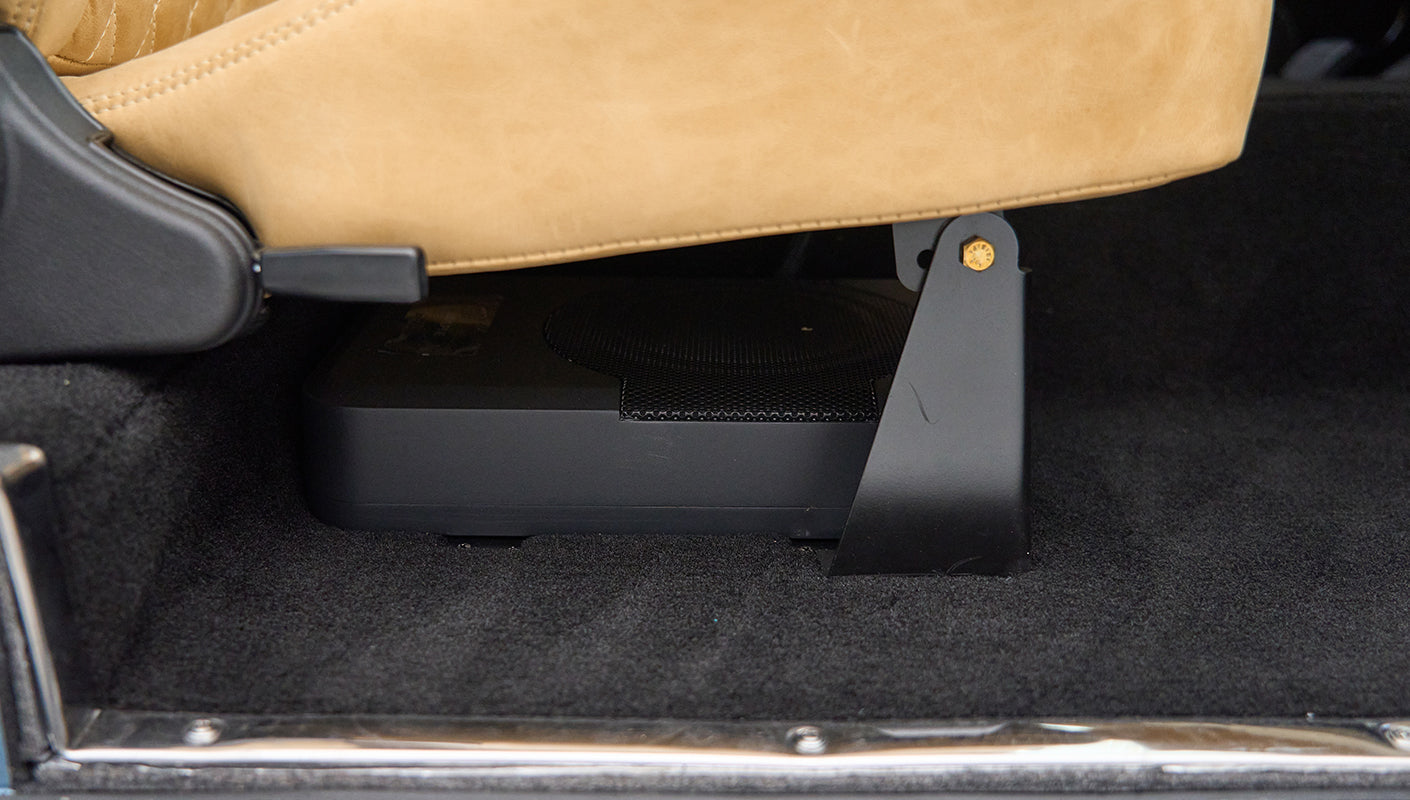 Black subwoofer speaker box installed under tan seat inside Classic Ford Bronco