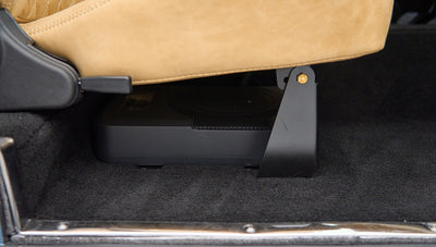 Black subwoofer speaker box installed under tan seat inside Classic Ford Bronco