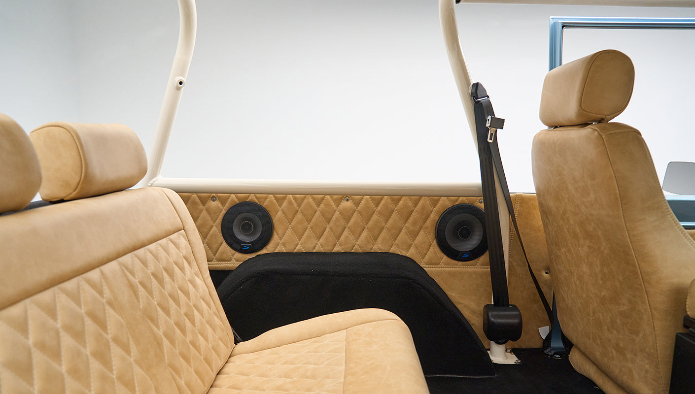 Wide view of Classic Ford Bronco interior rear seats with tan quilted upholstery and black speaker covers on side panels
