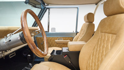 Driver side view of wood steering wheel and beige leather seating in Classic Ford Bronco