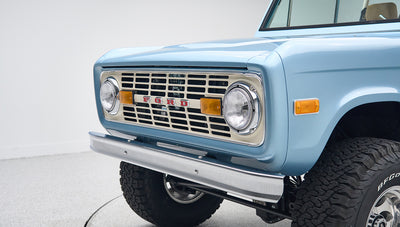 Close-up front view of light blue Classic Ford Bronco grille with FORD lettering and round headlights