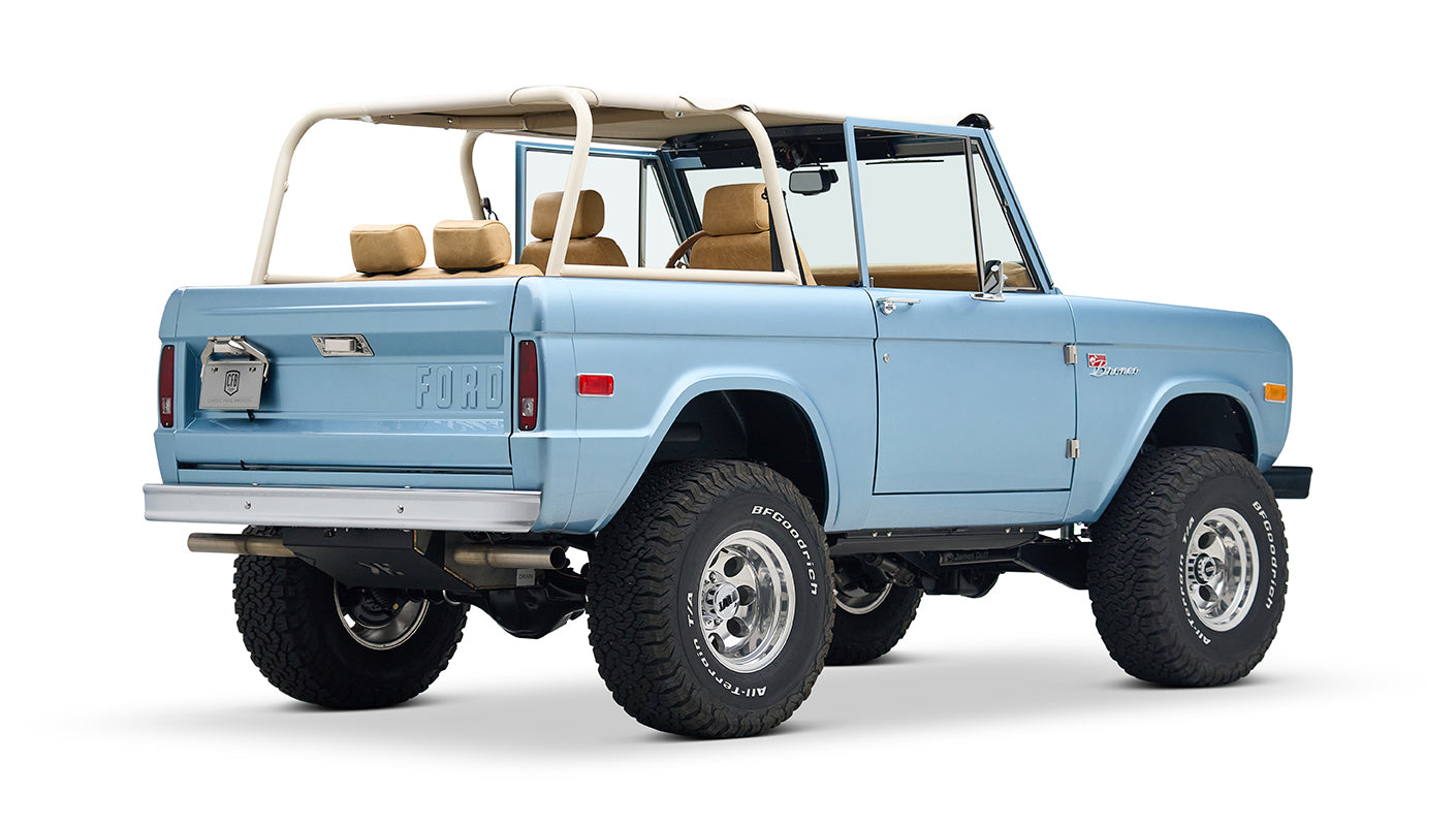 Light blue Classic Ford Bronco with beige roll cage, three-quarter left rear view showing tailgate