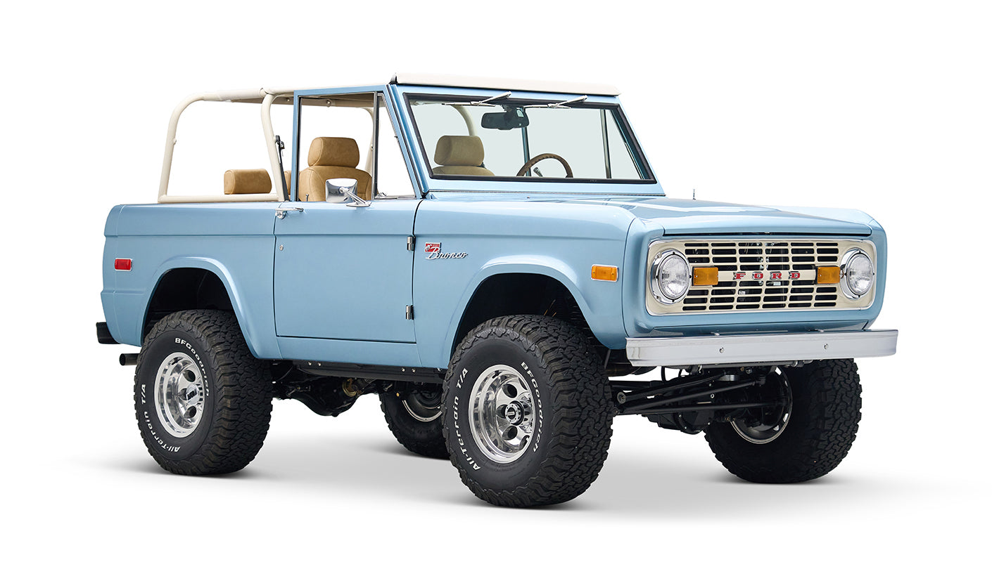 Light blue Classic Ford Bronco with tan seats and white roll cage, three-quarter left front view