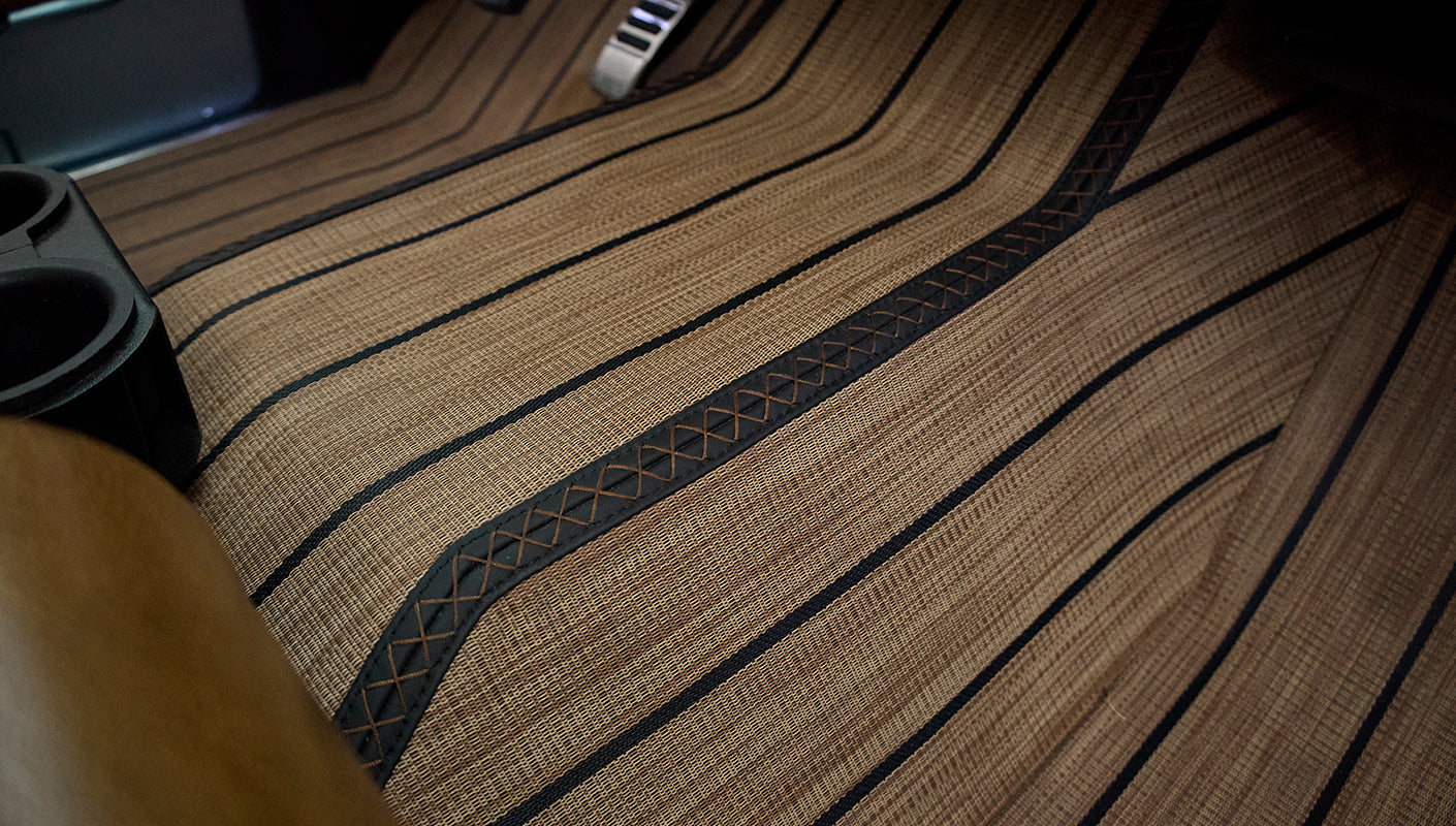 Tan woven floor mats with black trim covering vehicle floor between seats and beneath console