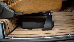 Underneath brown leather car seat showing electronic device mounted under the seat on tan floor mat