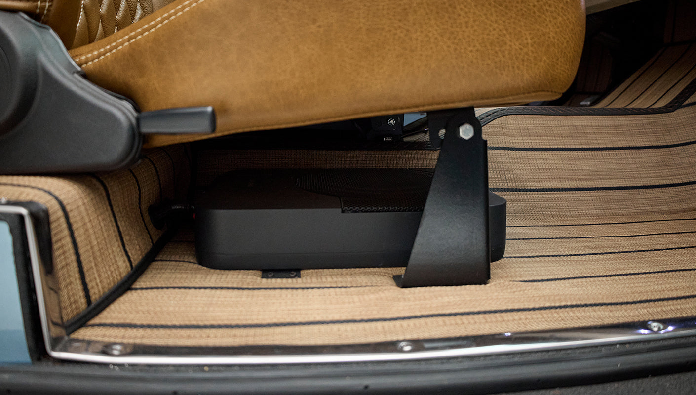 Underneath brown leather car seat showing electronic device mounted under the seat on tan floor mat
