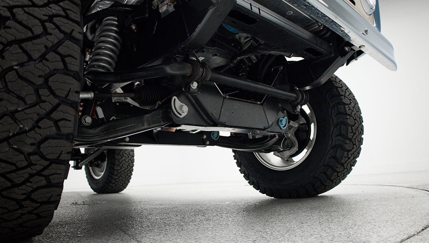 Close-up of vehicle undercarriage showing suspension parts and off-road tires on white floor