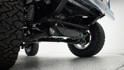 Close-up of vehicle undercarriage showing suspension parts and off-road tires on white floor