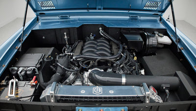 Front view under raised hood showing Classic Ford Bronco engine and surrounding components in blue engine bay