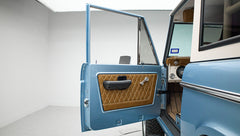 Open driver-side door of Classic Ford Bronco revealing quilted tan door panel and part of interior