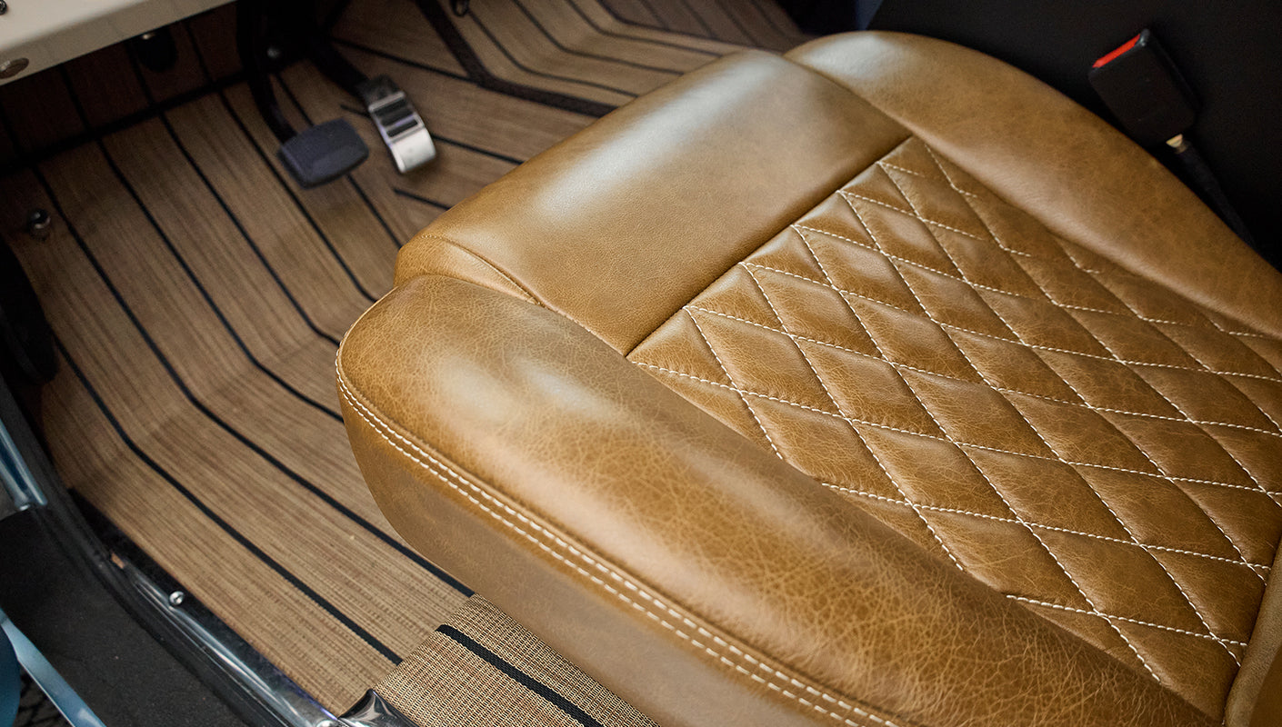Brown leather seat with quilted stitching and striped floor mat inside Classic Ford Bronco