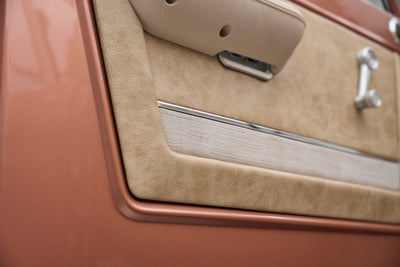 Interior door panel of a Classic Ford Bronco in beige and bronze tones with manual window crank.