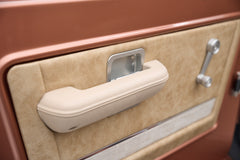 Beige interior door handle and armrest of a Classic Ford Bronco with bronze door panel.