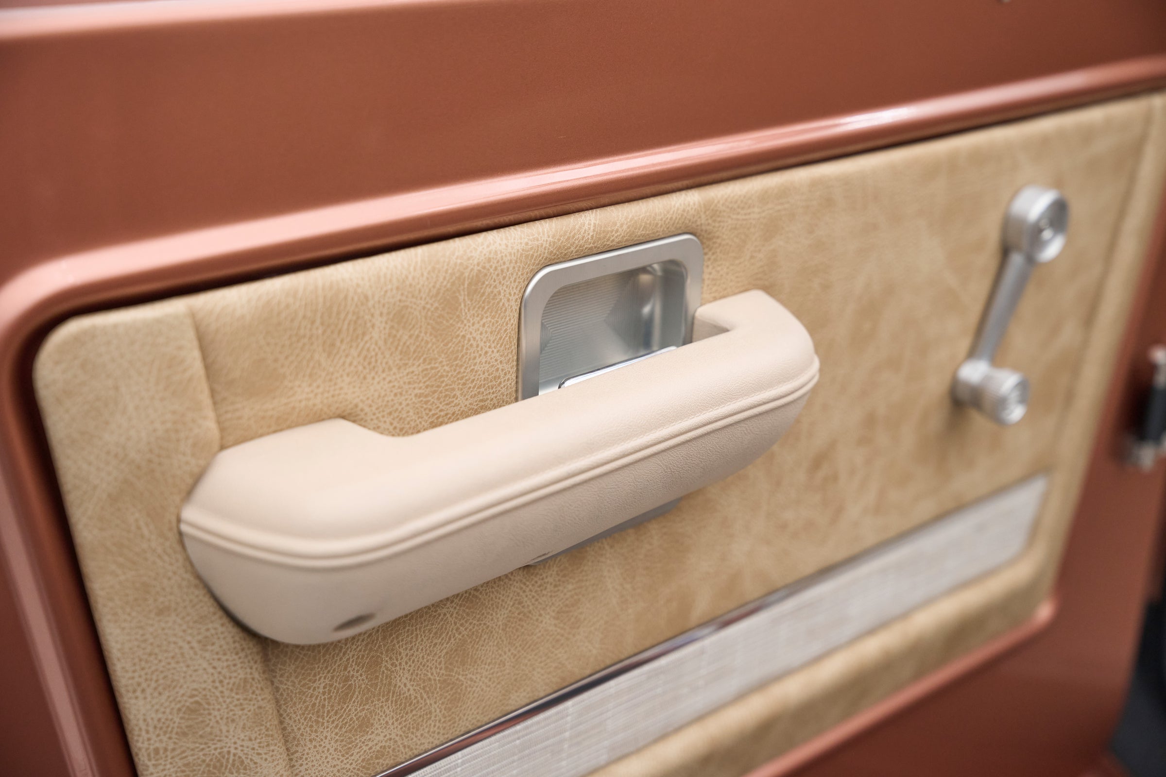 Beige interior door handle and armrest of a Classic Ford Bronco with bronze door panel.