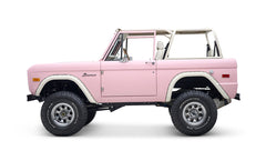 Side profile of pink Classic Ford Bronco with white roll cage and large BFGoodrich tires
