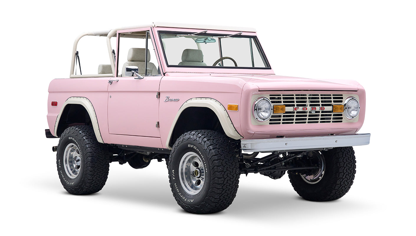 Front three-quarter view of pink Classic Ford Bronco showing grille, round headlights, and lifted stance