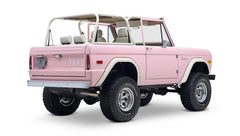 Rear three-quarter view of pink Classic Ford Bronco with white roll cage and dual exhaust pipes