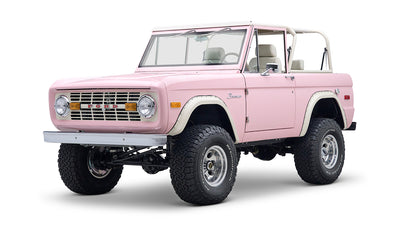 Front three-quarter view of pink Classic Ford Bronco showing grille, headlights, and front suspension