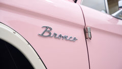 Close-up of chrome 'Bronco' emblem on pink Classic Ford Bronco door