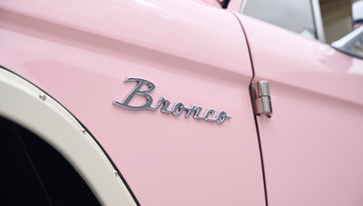 Close-up of chrome 'Bronco' emblem on pink Classic Ford Bronco door