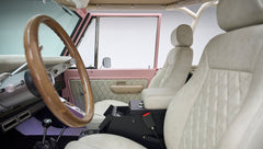 Interior of Classic Ford Bronco showing white quilted seats, wood steering wheel, and door panel details
