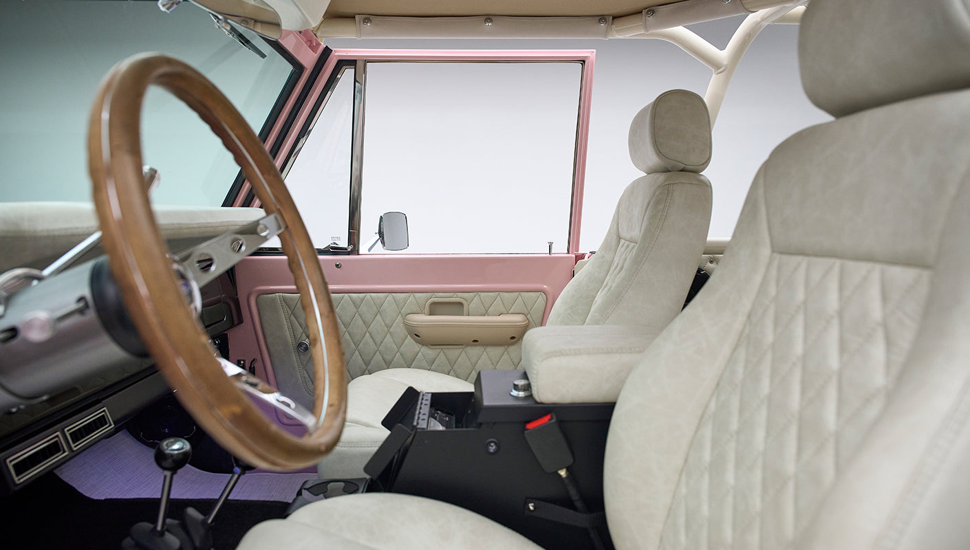 Interior of Classic Ford Bronco showing white quilted seats, wood steering wheel, and door panel details
