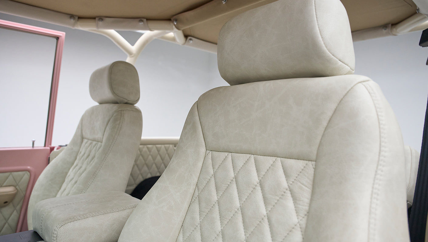 Light beige diamond-stitched driver's seat and armrest inside a Classic Ford Bronco with a pink door frame