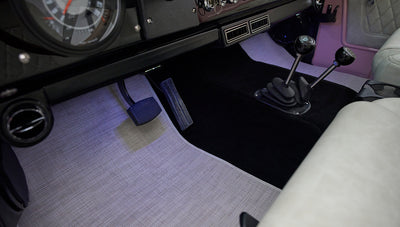 Foot pedals and two gear levers on black carpet floor with beige and black surrounding in a Classic Ford Bronco