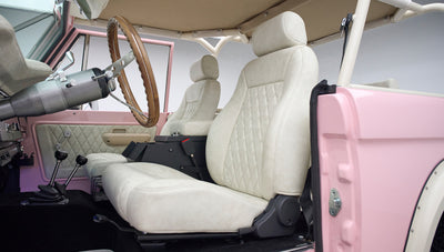 Side view of two diamond-stitched beige front seats and wooden steering wheel inside a Classic Ford Bronco with pink door