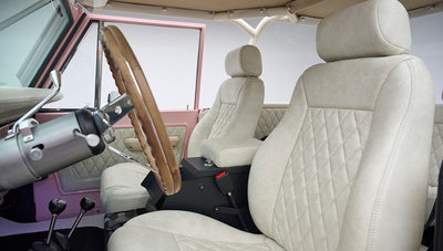 Driver and passenger diamond-stitched beige seats with wooden steering wheel and pink door interior in a Classic Ford Bronco