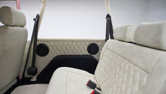 Rear diamond-stitched beige seats with black seat belts and speakers on side panels in a Classic Ford Bronco