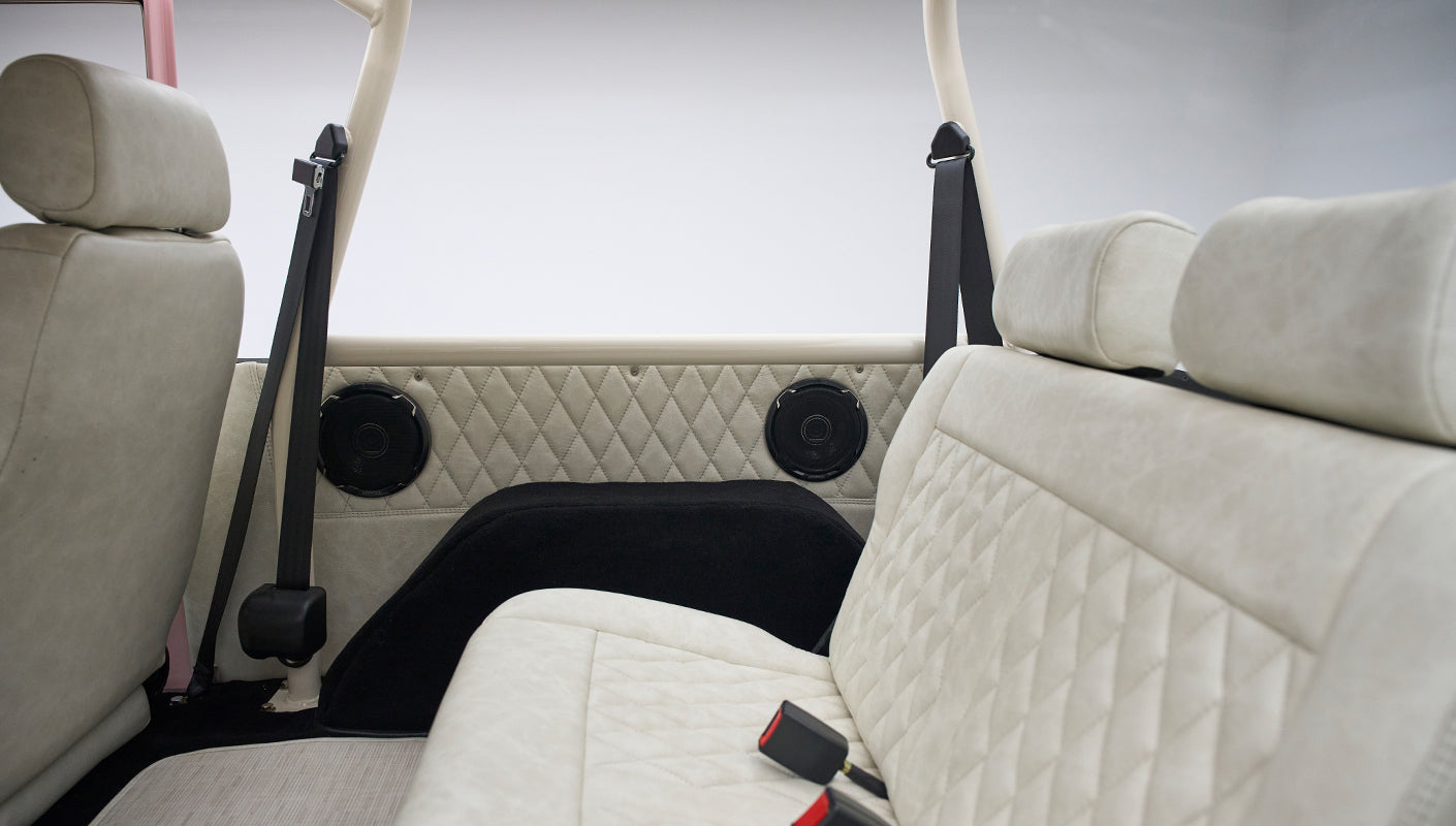 Rear diamond-stitched beige seats with black seat belts and speakers on side panels in a Classic Ford Bronco